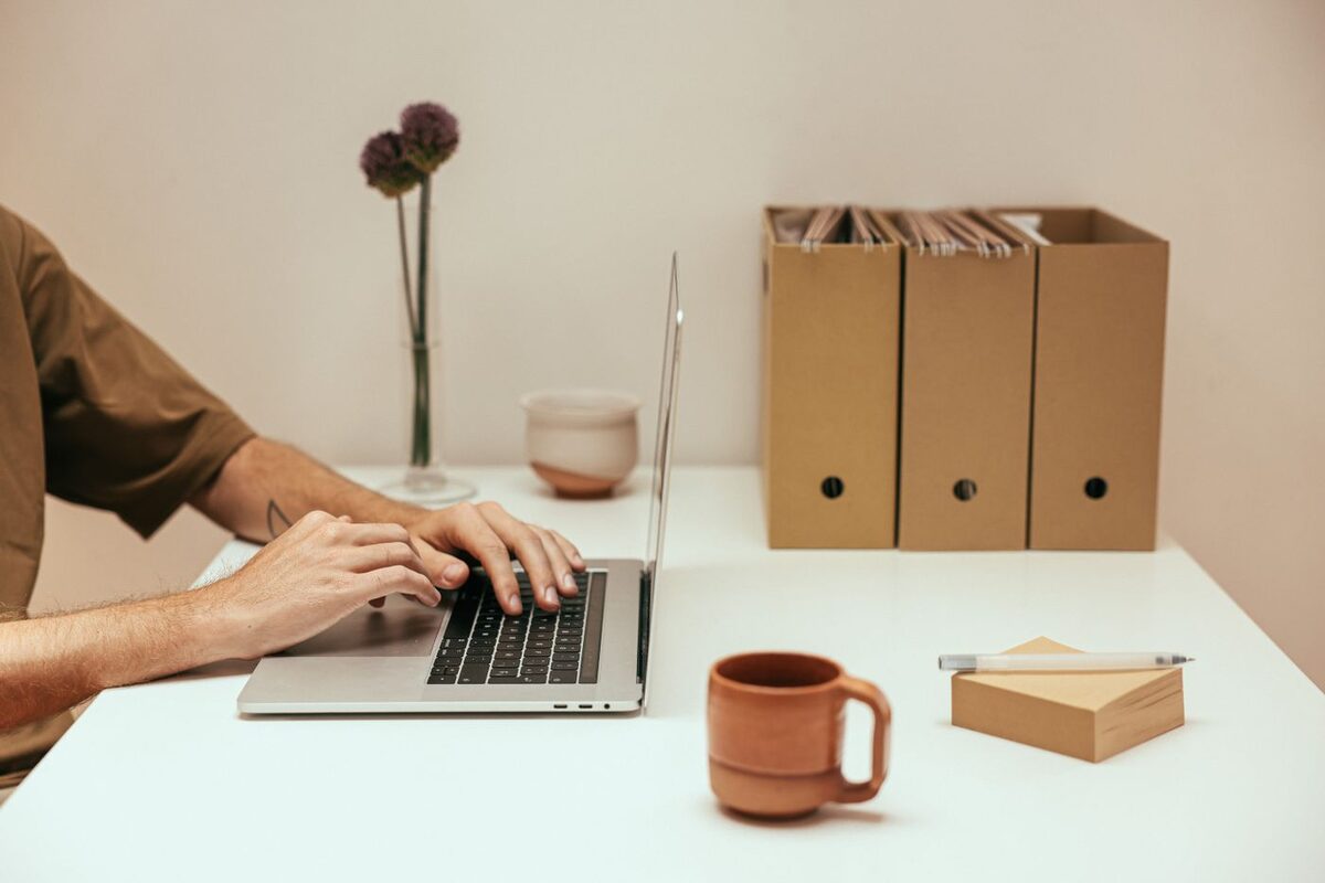 Someone working at a laptop on an ordinary desk beside cardboard file boxes